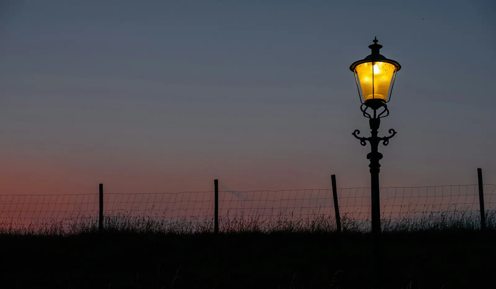 Poste de luz e cerca em silhueta contra o céu rosa do entardecer