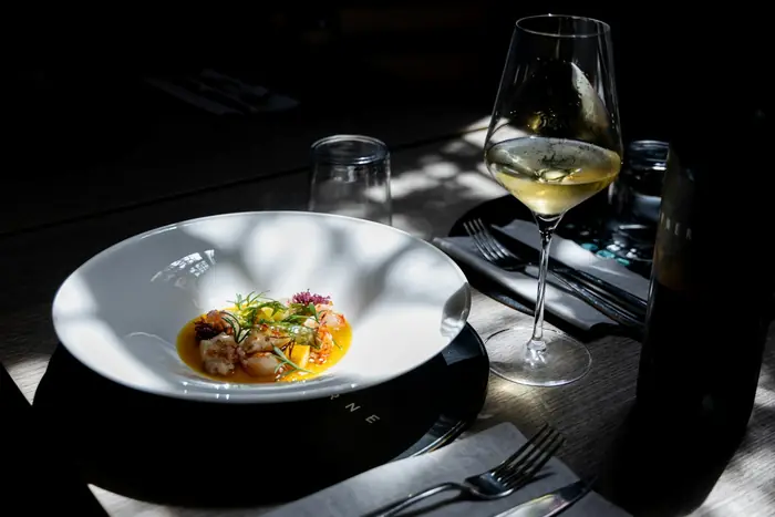 Prato autoral servido com vinho branco, sob luz natural