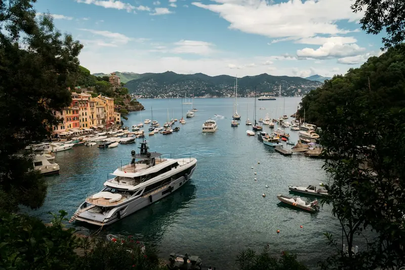 Marina numa baía, com iate, barcos atracados e a vila na encosta