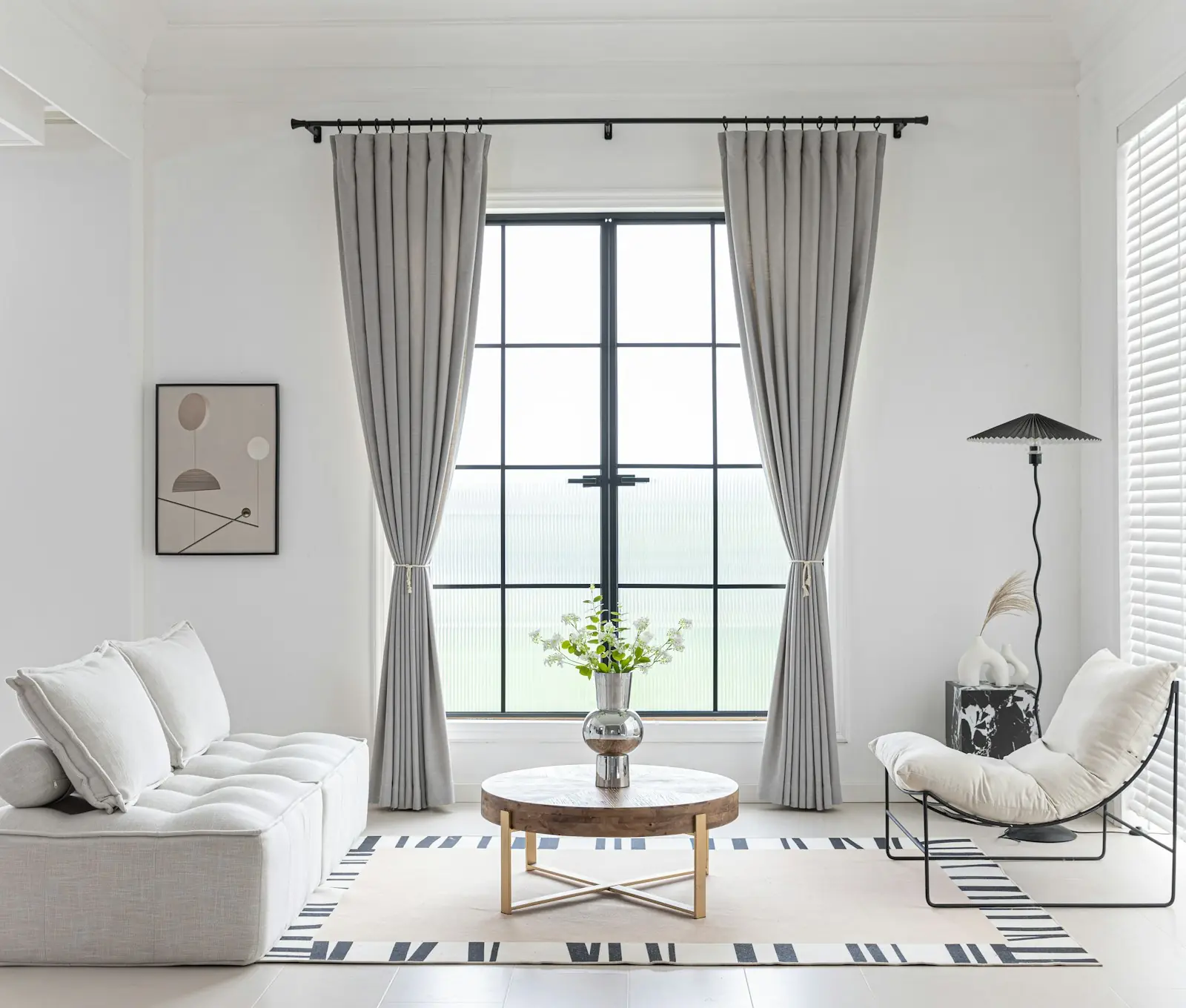 Sala clara com janela ampla e cortinas leves, sofá e poltrona brancos