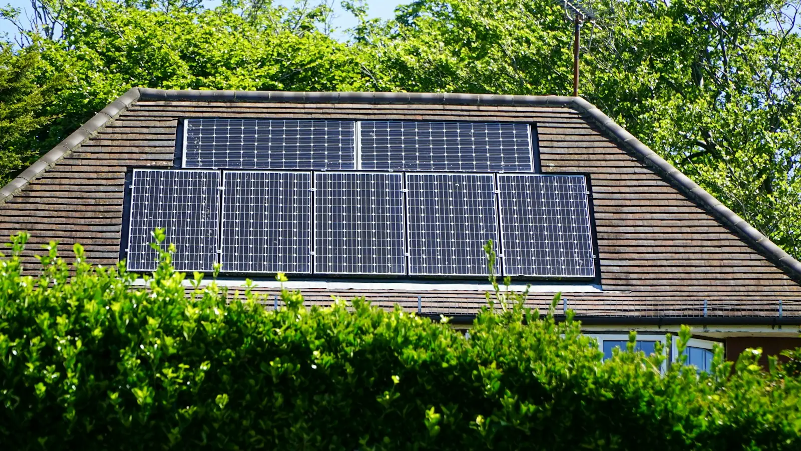 Painéis solares no telhado de uma casa, emoldurados por cerca-viva e árvores